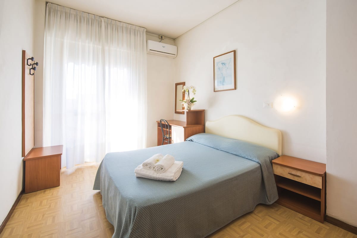 A neatly arranged bedroom with a bed, bedside tables, a mirror, and a window with curtains.