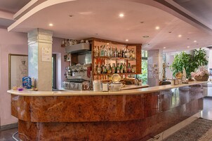 Zona de bar con mostrador de mármol, estantes llenos de botellas de licores y una cocina al fondo.