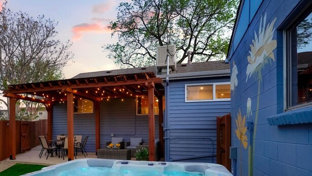 Een achtertuin met een jacuzzi, buitenmeubels en een pergola met lichtslingers.