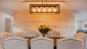 Een eethoek met een houten wand, een kroonluchter en een bloemenvaas op de tafel.