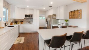 Een moderne keuken met witte kasten, een centraal kookeiland met barkrukken, een magnetron en een koelkast.
