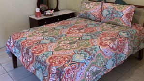 A bedroom with a patterned bedspread, a wooden dresser with a mirror, and a green pillow. - Studio Apartment in Negril - 2 minutes walk from the Community Beach! (Negril)