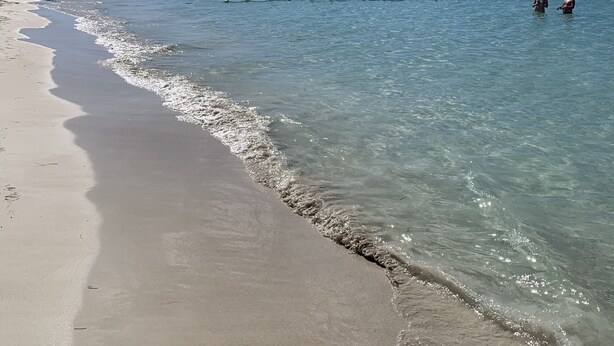 A beach with clear water, a sandy shore, and a distant shoreline with boats. - Studio Apartment in Negril - 2 minutes walk from the Community Beach! (Negril)