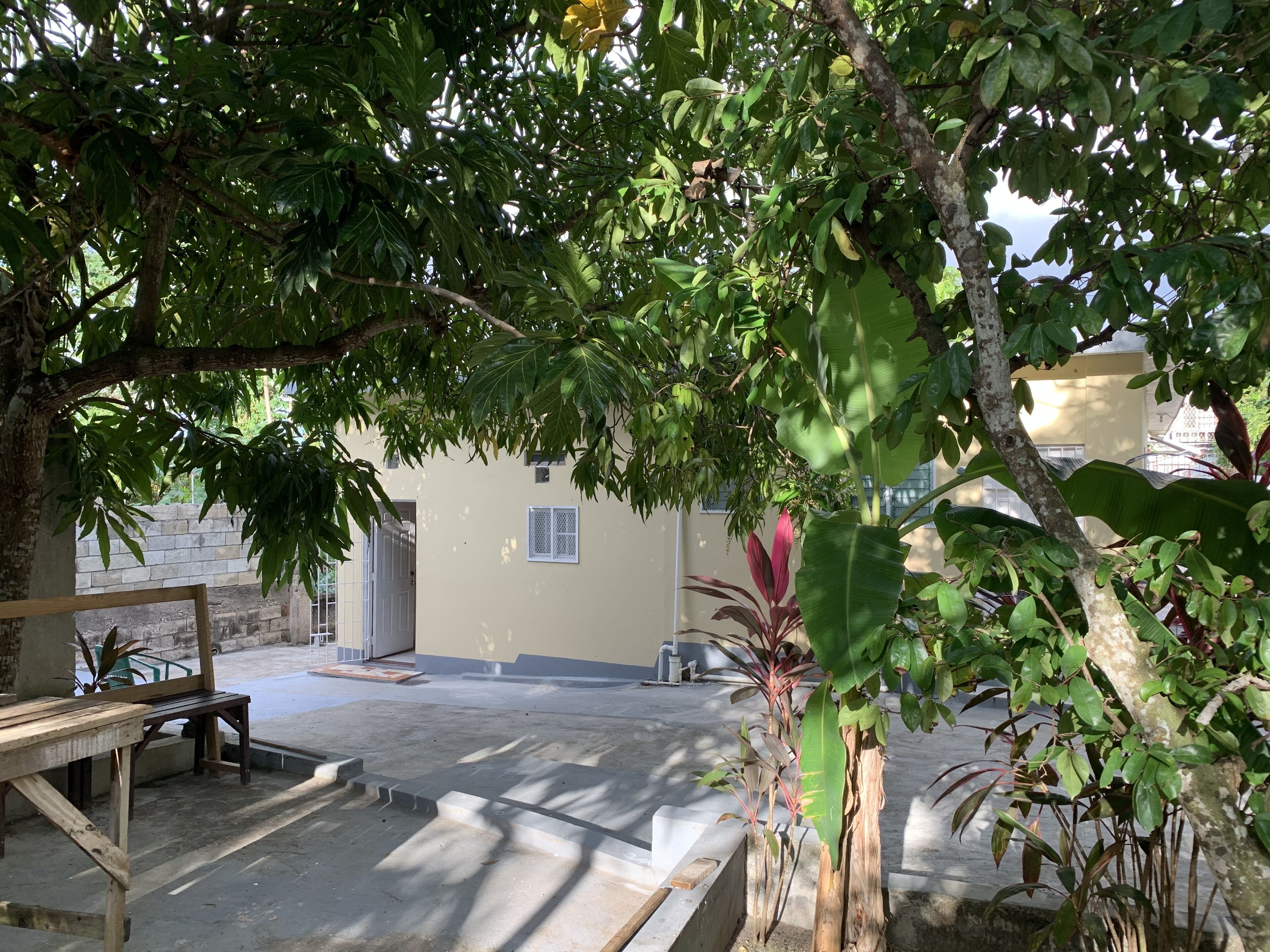 A courtyard with a wooden bench, a concrete pathway, and a building with a window and a door.