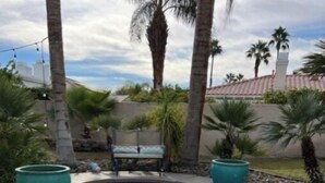 A swimming pool with a stone edge, surrounded by palm trees and a bench.