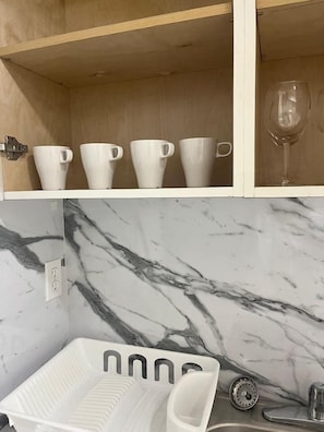 A kitchen with a marble backsplash, a white sink, and a countertop with a dish rack. - Modern Apartment| City Views + Easy Beach Access (Miami)
