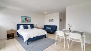 A bedroom with a bed, bedside tables, a desk, chairs, and a painting on the wall. - Modern Apartment| City Views + Easy Beach Access (Miami)