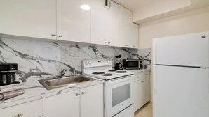 A kitchen with white cabinets, a marble backsplash, a stove, a sink, a microwave, and a refrigerator. - Modern Apartment| City Views + Easy Beach Access (Miami)
