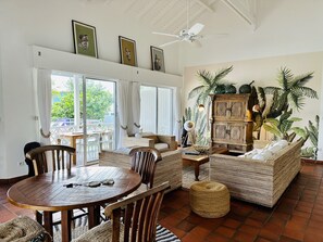 Amplia zona de estar con una mesa redonda de madera, muebles de mimbre y una pared cubierta de plantas.