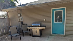 A barbecue grill with a chair and a table in front of a house with a blue door. - Lovely Guest Cottage min from Perdido Key Beaches (Pensacola)
