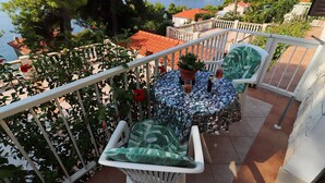 A balcony with a white railing, a table with a stone-patterned tablecloth, a chair with a green cushion, and a potted plant. - Seaside Apartments Markota - Studio Apartment with Sea View (Prižba)