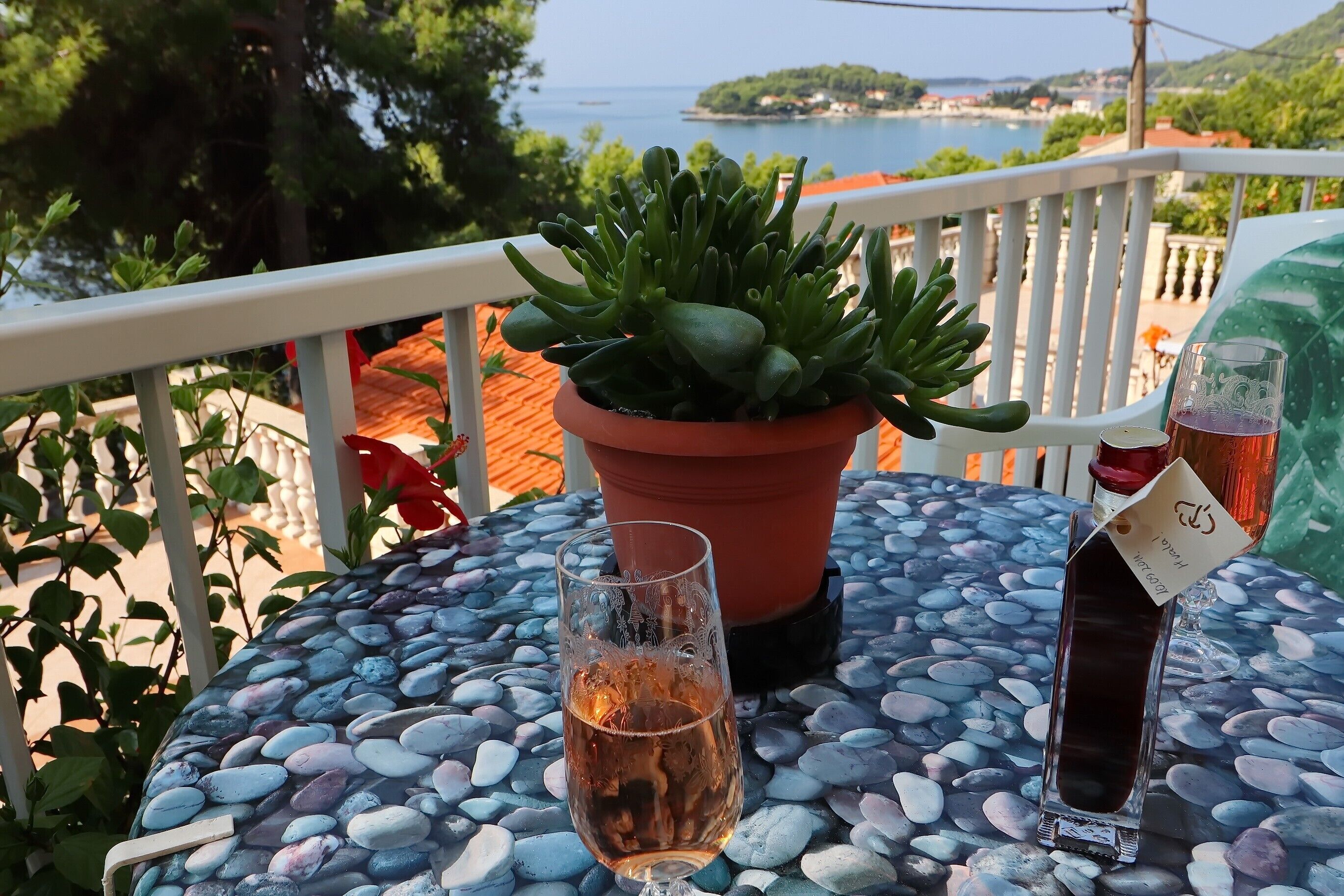 Ein Tisch mit einer Topfpflanze, einem Weinglas und einer Weinflasche im Freien auf einer Kiesunterlage.