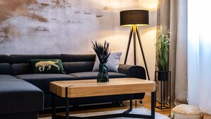 Un salon moderne avec un canapé d’angle, une table basse en bois, un lampadaire et une plante en pot.