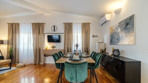 Un espace de salle à manger moderne avec une table en bois dressée pour six personnes, des chaises à revêtement vert et une console noire adossée au mur.