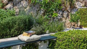 Een stenen muur met verschillende planten en een bank met boeken en een kussen.