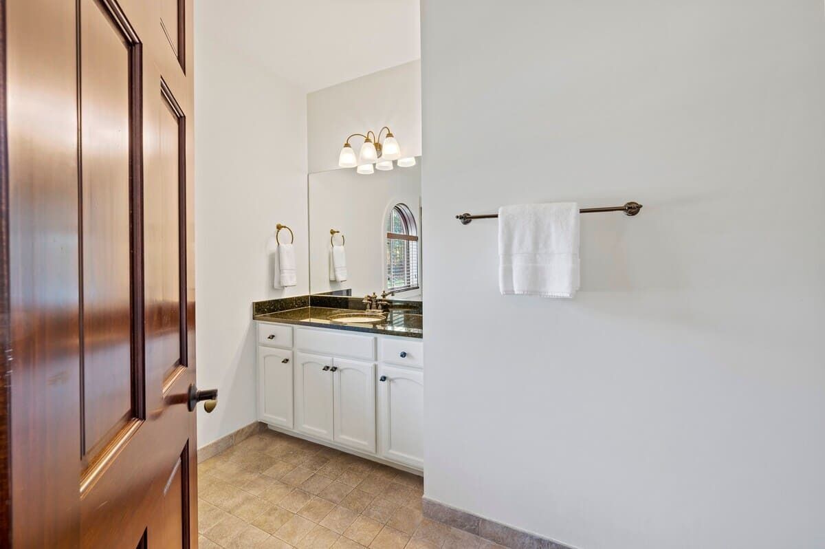 A bathroom with a wooden door, white cabinets, a sink with a mirror, and a towel rack.