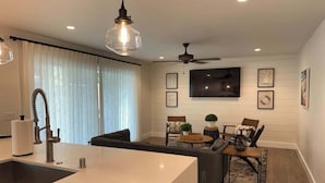 Una cucina moderna con isola centrale, un'area pranzo con tavolo e sedie, una ventola a soffitto e un televisore a schermo piatto montato a parete.
