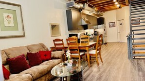 Un salon avec un canapé, une table basse en verre, des chaises en bois, une table à manger et, au fond, une cuisine.