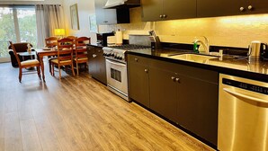 Une cuisine moderne avec des meubles de couleur sombre, des appareils en acier inoxydable et un coin repas en bois comprenant une table et des chaises.
