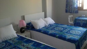 Ein Hotelzimmer mit zwei Einzelbetten, einem kleinen Tisch mit Stuhl, einer Lampe und einem Fenster mit gemusterten Vorhängen.