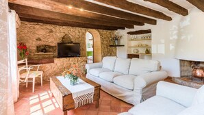 A cozy living room with a stone wall, a white sofa, a wooden coffee table, and a fireplace. - Villa with jacuzzy in Pollensa town (Pollensa / Pollença)