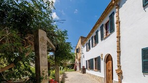 A narrow cobblestone street flanked by white buildings with green shutters, a stone archway, and lush greenery. - Villa with jacuzzy in Pollensa town (Pollensa / Pollença)