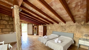 A spacious bedroom with two beds, a stone wall, and a wooden ceiling. - Villa with jacuzzy in Pollensa town (Pollensa / Pollença)