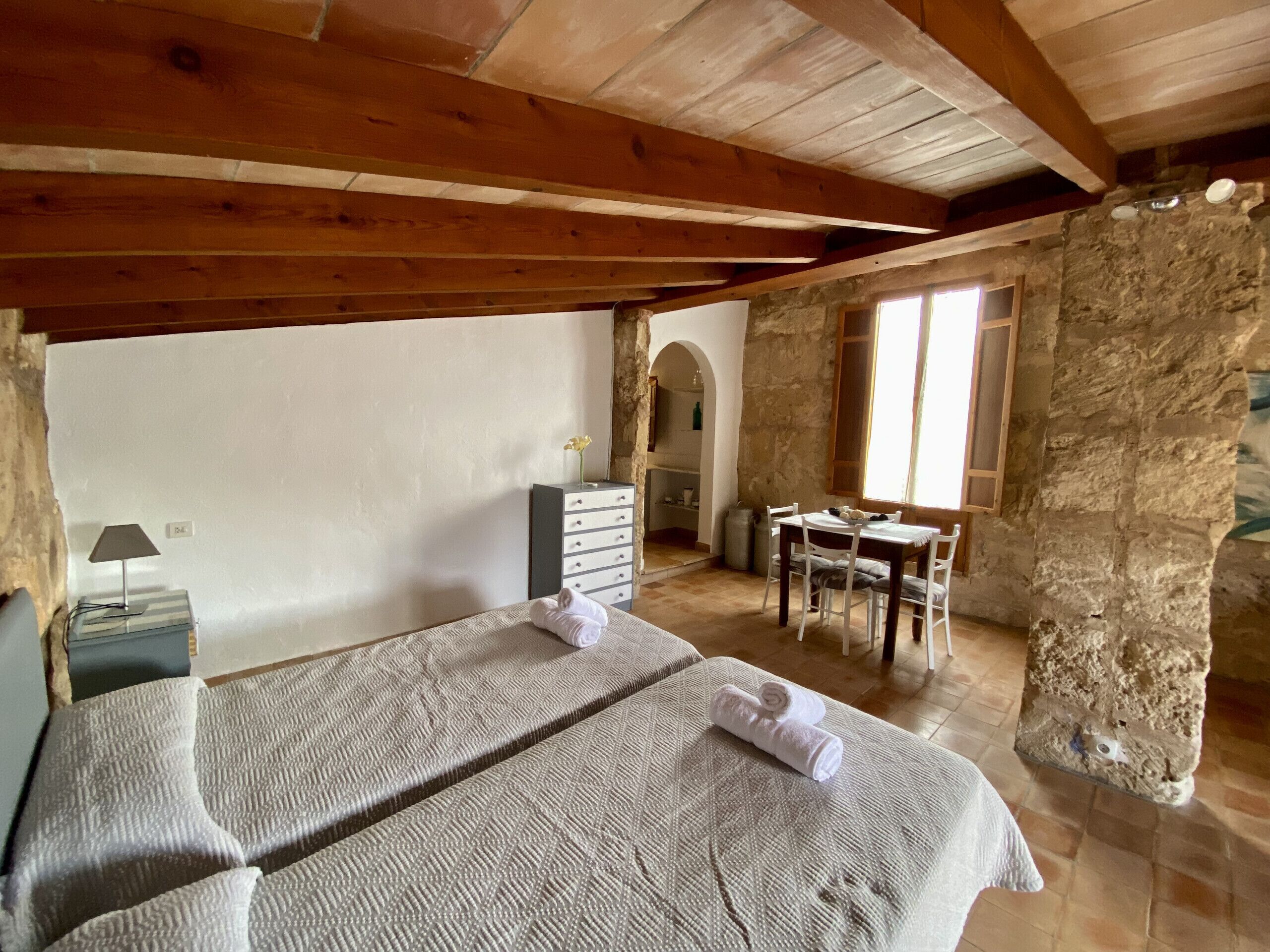 Une chambre à coucher avec un lit, un bureau et une chaise. Il y a un mur en pierre et un plafond en bois.