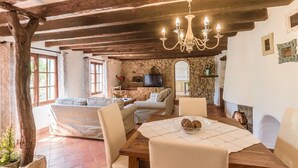A rustic interior with exposed wooden beams, a stone wall, a fireplace, a dining table with chairs, and a sofa set. - Villa with jacuzzy in Pollensa town (Pollensa / Pollença)