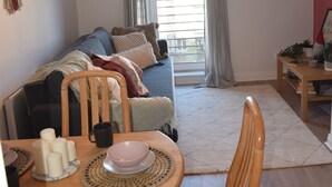 A cozy living room with a sofa, dining table, and chairs. There is a window with curtains, a hanging light fixture, and a small side table with a plant. - Cozy Dublin City Apt near Guinness Storehouse and Temple Bar (Dublin)