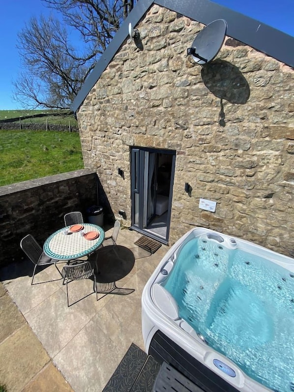 A stone building with a hot tub, a table with chairs, and a satellite dish.