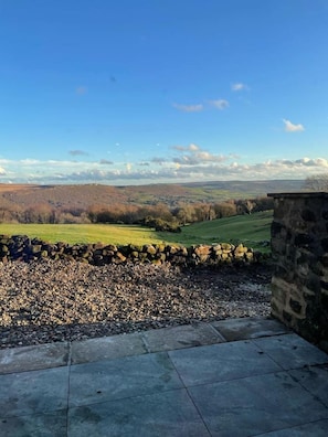 A stone wall and a paved area leading to a scenic view of rolling hills and a clear sky.