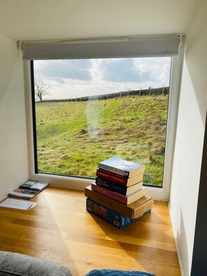 A room with a large window, a stack of books, and a wooden floor. - The Barn Grown-up Peaceful Stay with Far-Reaching Views (Eyam)