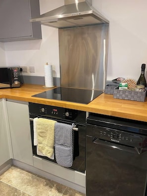 A kitchen with a stainless steel range hood, a microwave, a dishwasher, and a wooden countertop.