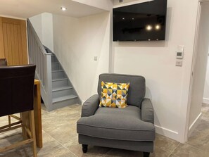 A living room with a grey sofa, a patterned throw pillow, a flat-screen TV mounted on the wall, and a staircase in the background. - The Barn Grown-up Peaceful Stay with Far-Reaching Views (Eyam)