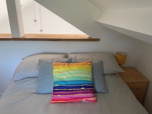 A bedroom with a bed, pillows, a bedside table, and a window.