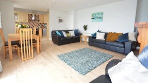 A living room with a black sofa, a grey sofa, a wooden dining table with chairs, a small coffee table, and a blue patterned rug. - Ballycotton Holiday Apartment No 6 (Ballycotton)