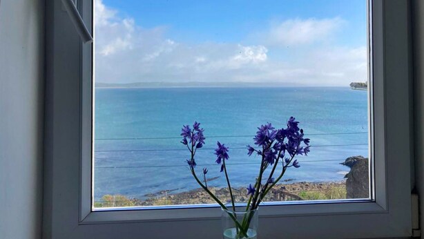 A window with a clear view of the sea and a vase with purple flowers. - Ballycotton Holiday Apartment No 6 (Ballycotton)