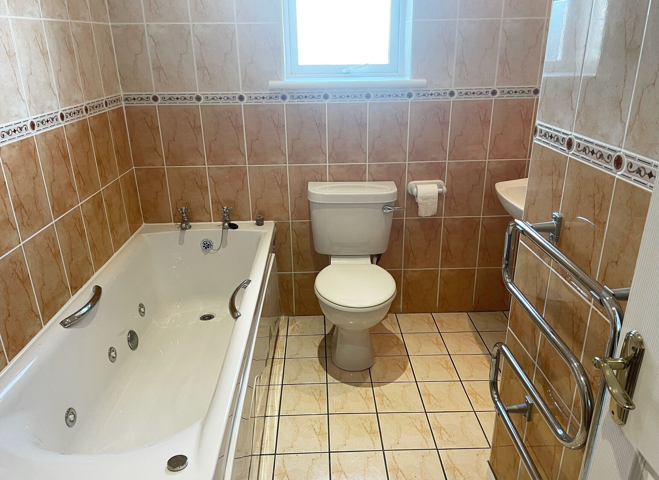 A bathroom with a bathtub, toilet, and handrail.