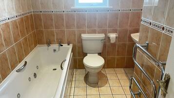 A bathroom with a bathtub, toilet, and handrail.