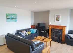 A living room with a black leather sofa, a wooden coffee table, a fireplace, a television, and artwork on the walls.