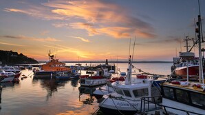 A marina with various boats docked, a sunset in the background, and a hilly landscape across the water. - Ballycotton Holiday Apartment No 6 (Ballycotton)