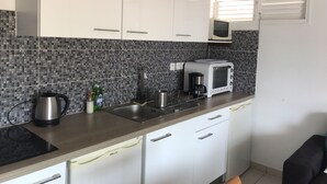 A modern kitchen with white cabinets, a black countertop, a microwave, a kettle, and a coffee maker. - Anse à l'âne apartment  (Les Trois-Îlets)