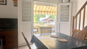 A room with a table and chairs, a TV, and a view of a building outside. - Anse à l'âne apartment  (Les Trois-Îlets)