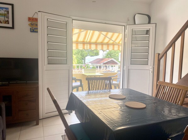 Une pièce avec une table et des chaises, un téléviseur et une vue sur un bâtiment à l’extérieur.
