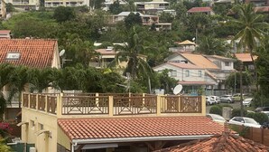 A residential area with houses, a balcony, and a view of a hill with more houses. - Anse à l'âne apartment  (Les Trois-Îlets)