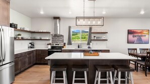 A modern kitchen with a central island, bar stools, a built-in stove, and a large window offering a view of the outdoors. - Townhome 47, 3 Bed-12 Guests with indoor/Outdoor pools+Rec Center at Waterdance (Garden City)