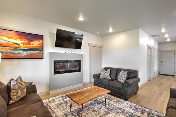 A living room with a fireplace, a large TV mounted above it, and a couch with patterned cushions.