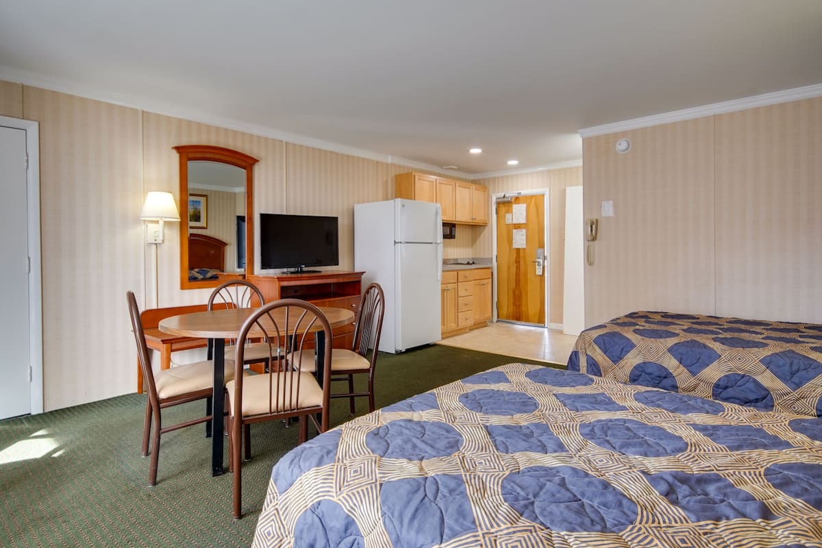 A compact hotel room with a bed, a dining table with chairs, a small kitchenette, and a television.