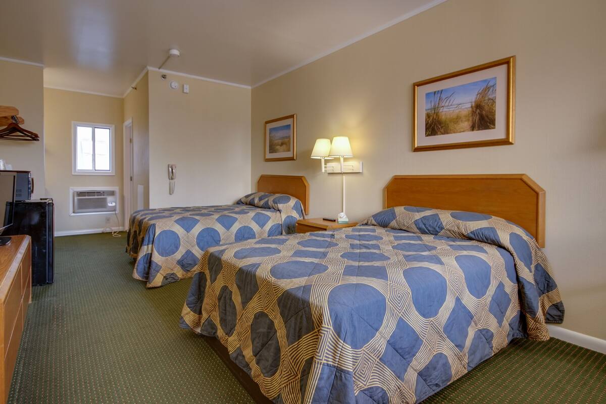 A hotel room with two beds, a desk, a lamp, and a painting on the wall.